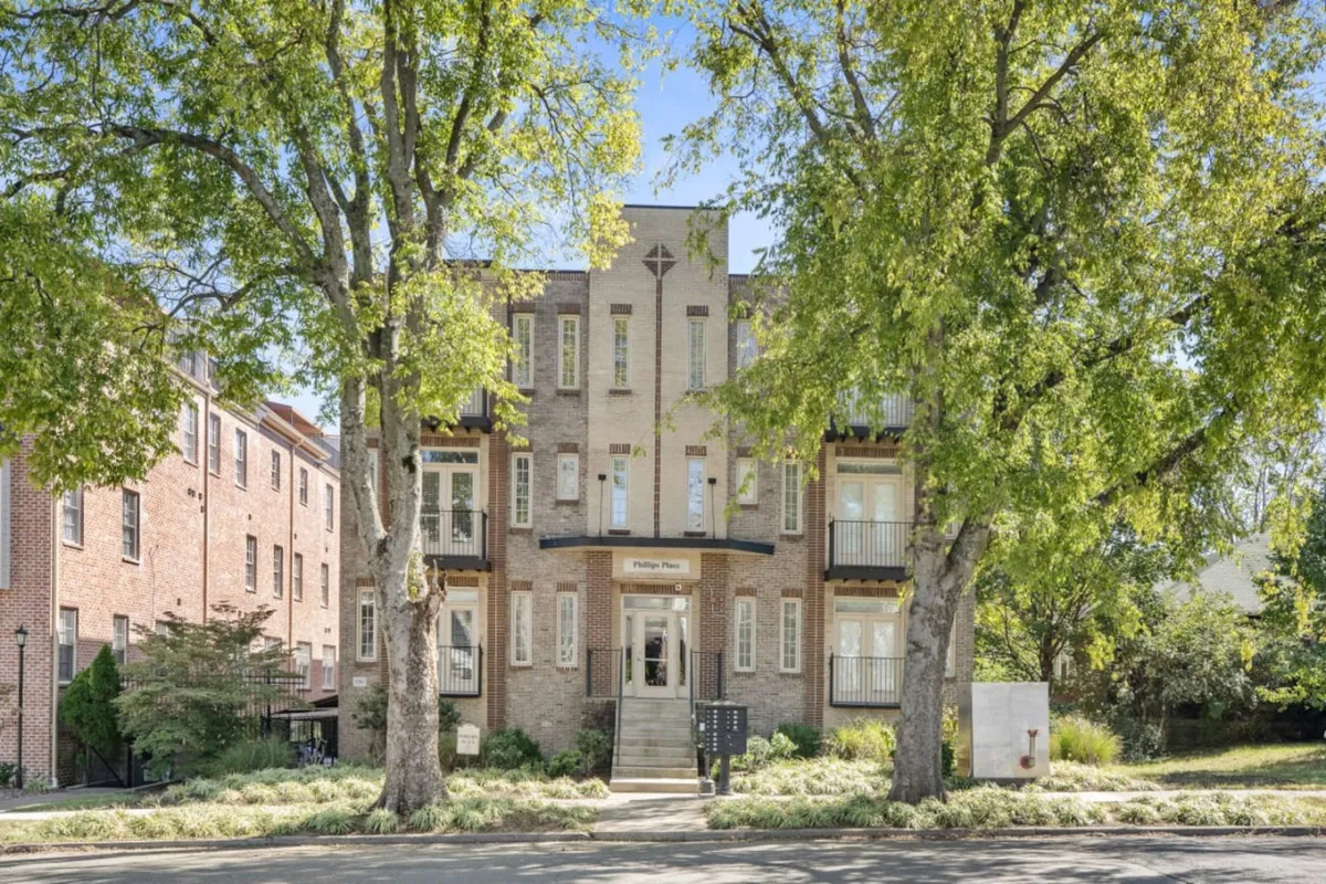 This exterior image captures the main entrance of the property, framed by large mature trees and showcasing a brick facade with decorative elements. The inviting front steps suggest a welcoming spot where residents and guests gather, setting the scene for neighborhood exploration.