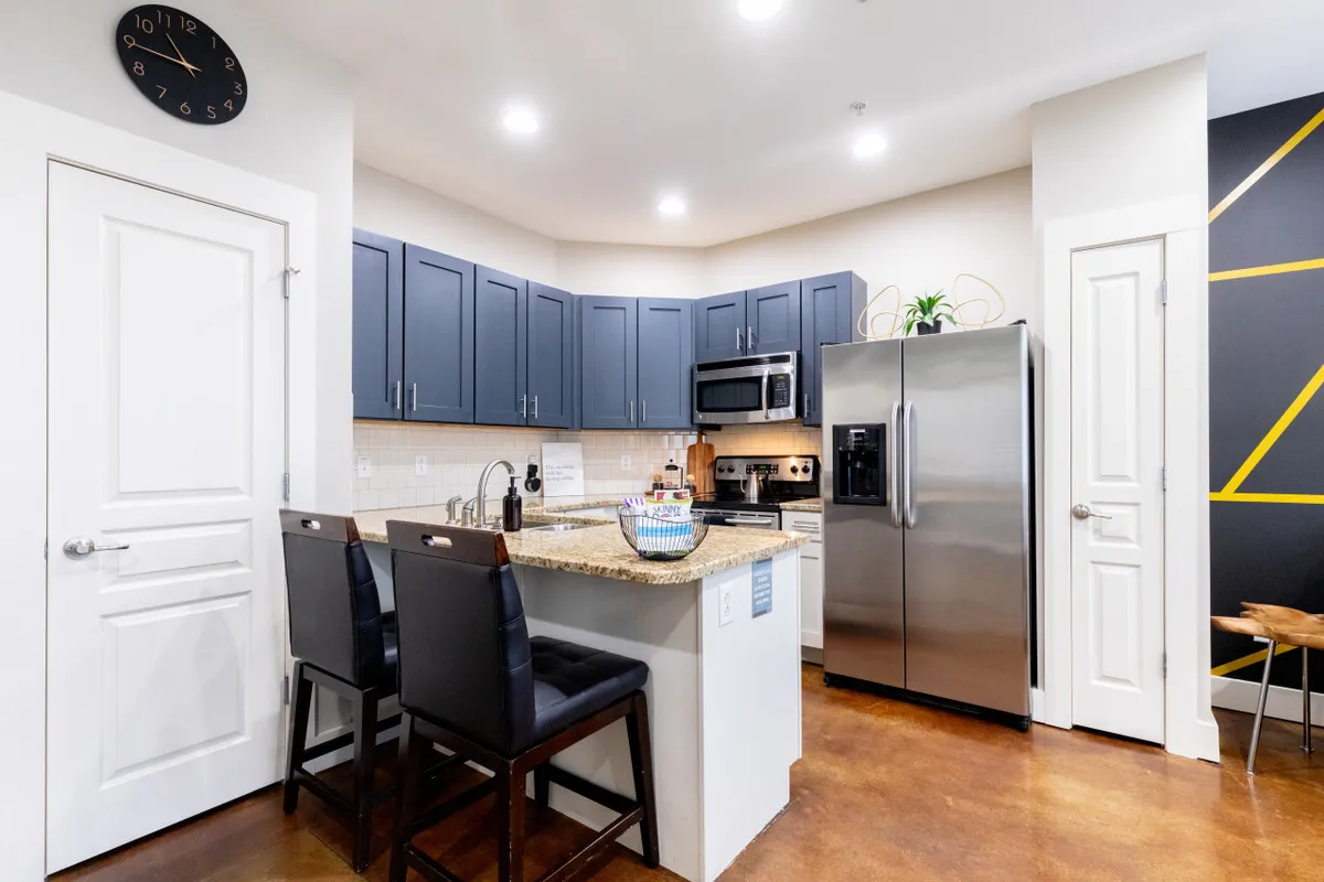 An inviting kitchen area showcasing a granite countertop, stainless steel oven and refrigerator, blue cabinetry, and a cozy seating area for sharing meals or sipping coffee. The layout encourages social interaction and communal dining.