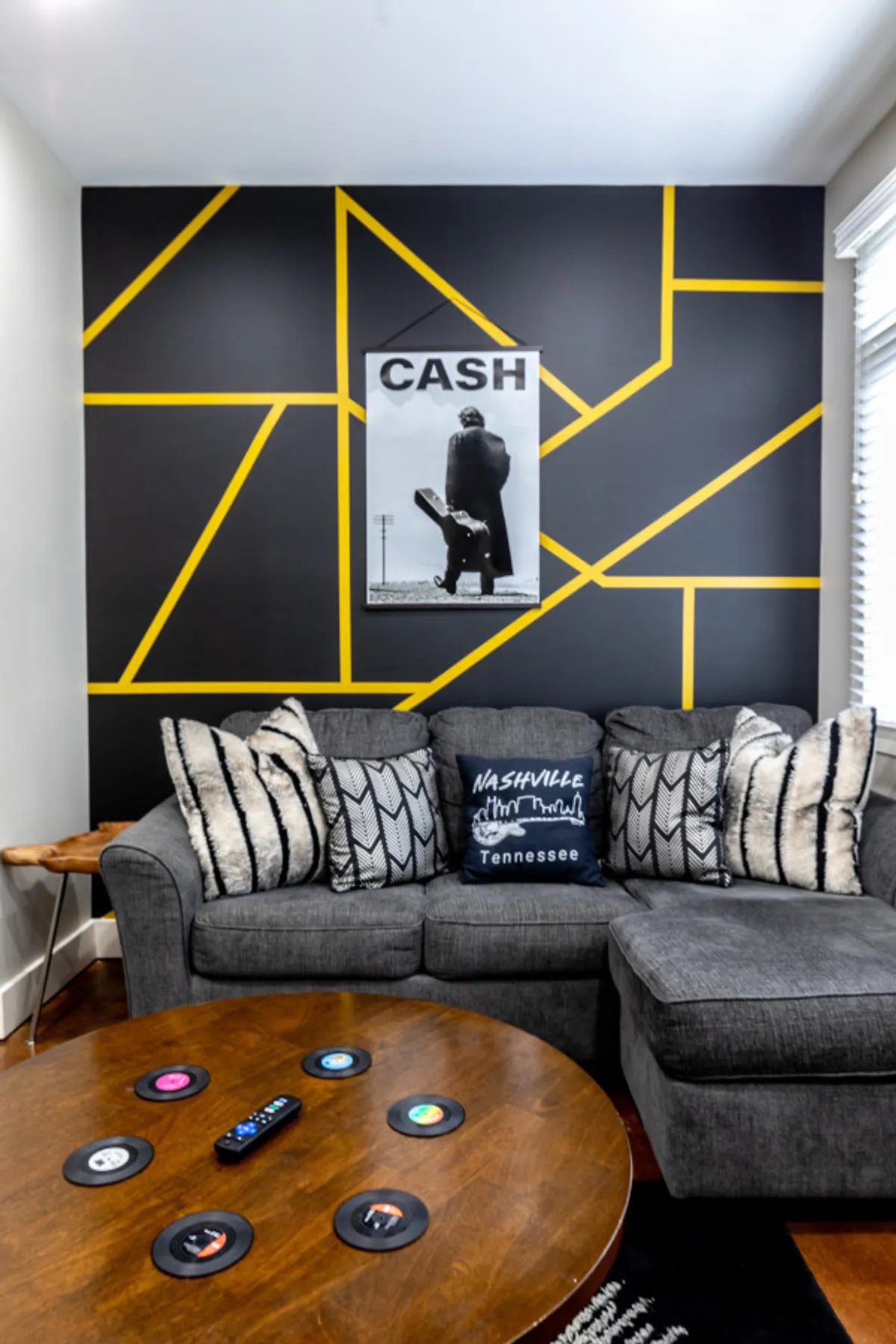 A vibrant living space with a large graphic art piece featuring a musician, a stylish couch with decorative pillows, and a unique coffee table topped with vinyl records. The room exudes a playful, artistic vibe tailored for music lovers and social gatherings.