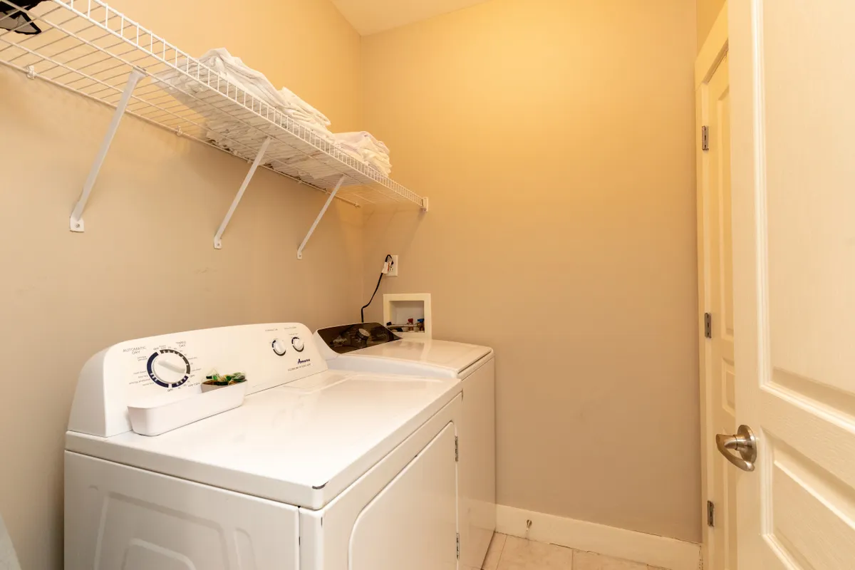 This image presents a dedicated laundry area with a washing machine, dryer, and neatly organized shelves stacked with fresh towels. The space is clean and practical, underscoring amenities that support longer, more comfortable family stays.