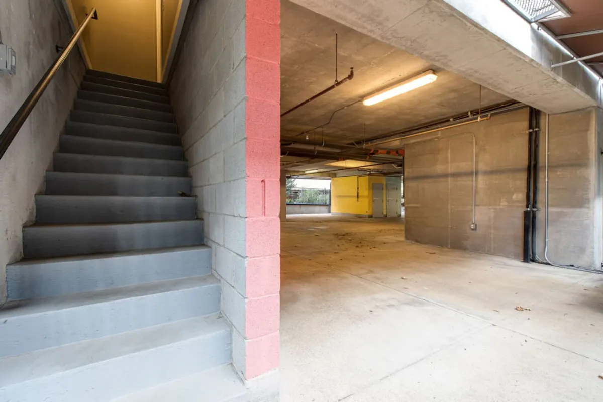 An industrial-chic interior garage space with a staircase, concrete walls, and open area for parking vehicles or storage, combining practicality with urban style.