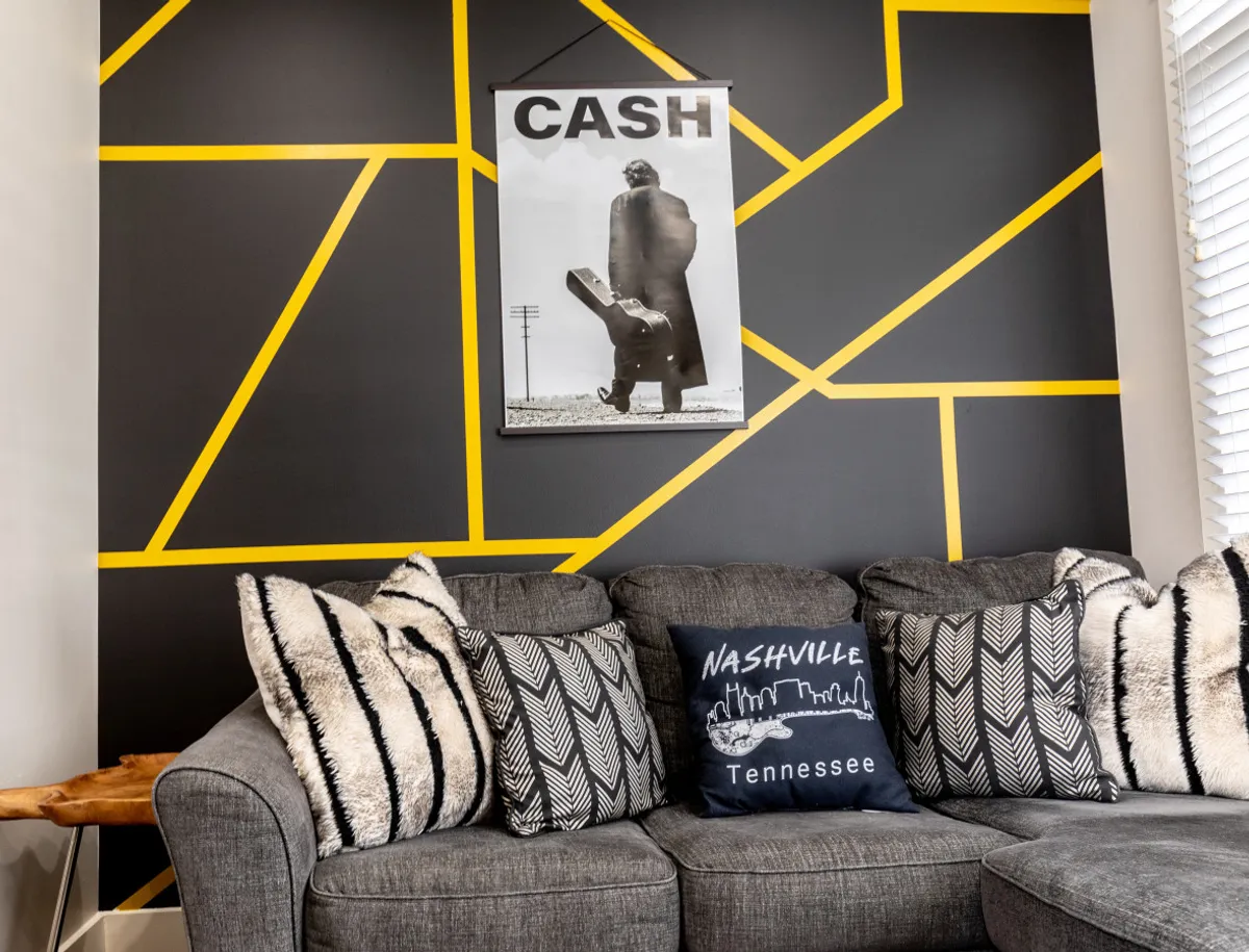 A cozy and contemporary space featuring Cash-themed artwork, a bold geometric wall design, and textured throw pillows. The room is set up for relaxing or entertaining, with subtle nods to Nashville and music culture.