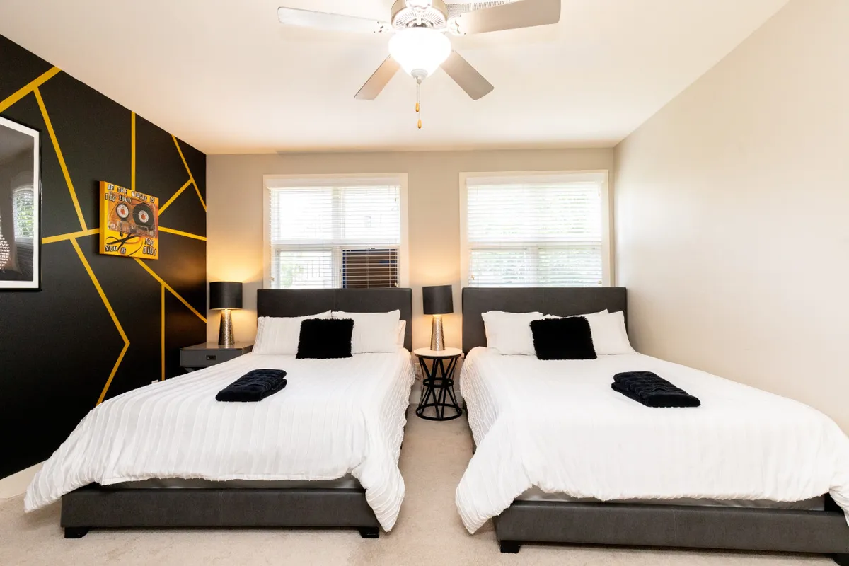 A stylish and modern bedroom showcasing two beds with geometric accent walls, decorative artwork, and bedside lamps. The overall look is inviting and tailored for relaxation and restful nights.