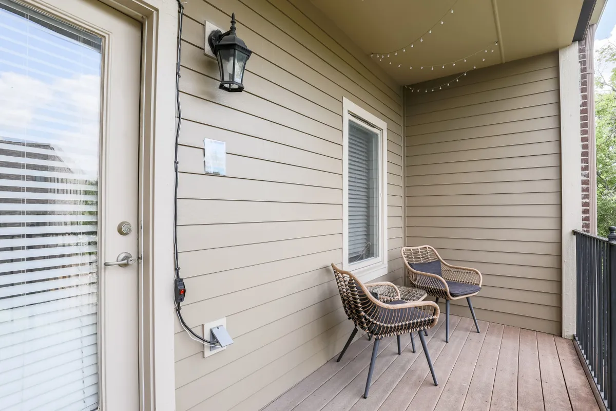 An inviting exterior scene featuring two wicker chairs on a private balcony or patio, with warm hanging lights and wood siding in the background. The setup is ideal for enjoying quiet mornings or relaxing evenings with a view.