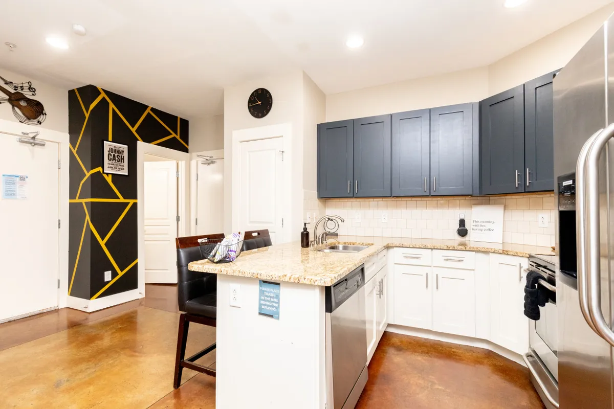 A contemporary kitchen with a granite countertop, dark blue cabinets, and a vibrant yellow accent wall. The kitchen is designed for cooking, entertaining, and casual dining, featuring modern finishes and a layout conducive to extended stays.
