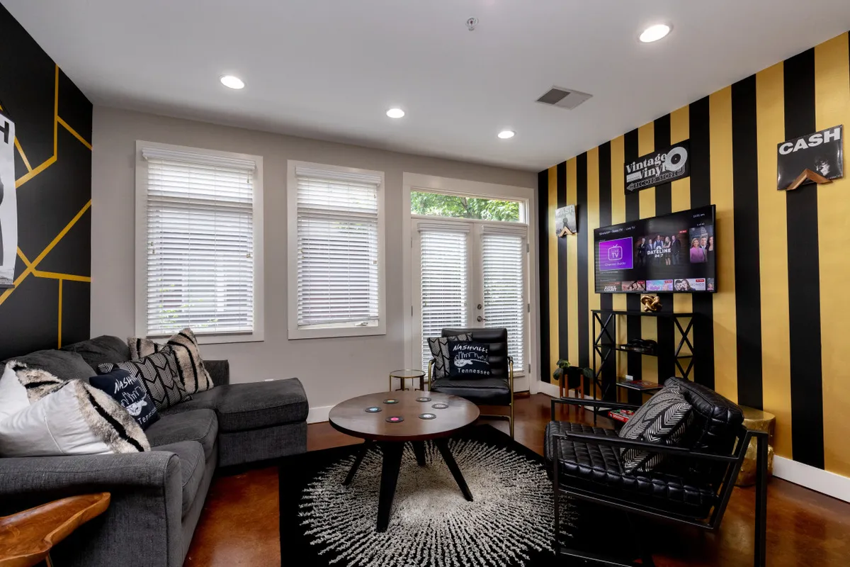 A cozy lounge setup with a comfortable sofa adorned with decorative pillows, a unique coffee table, vibrant striped wall art, and a TV displaying colorful content. The inviting space is ideal for movie nights, games, or simply enjoying each other’s company before heading out.