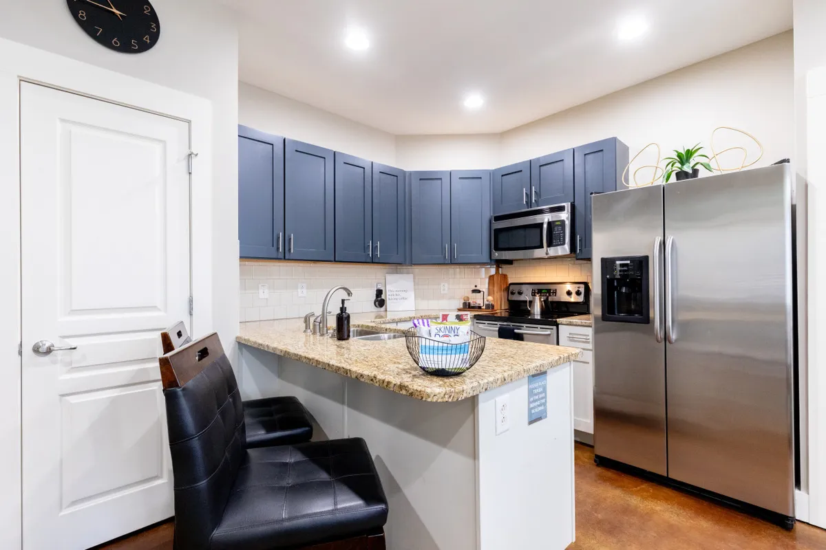 A modern kitchen with a striking granite countertop, sleek stainless steel appliances, rich blue cabinetry, and bar stools inviting guests to sit and chat. The space is well-lit and feels both functional and stylish, perfect for cooking or entertaining.